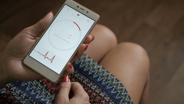 Woman Looking At Health Monitoring App On Smartphone. Monitoring the heart pulse with a health application on smartphone.