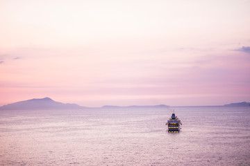 Touristic cruise boat in the middle of a quiet sea after the sunset with a pink coloured nice sky for all the people wander to travel and enjoy the vacation away home