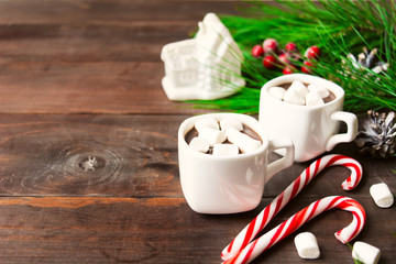 Two hot beverages with marshmallow in cups with toy house and two candy canes