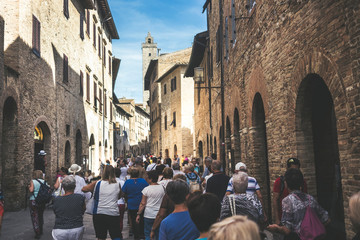 Crowd of tourists people walk together stretched and with the street full in San Gimignano near Siena in Tuscany, Italy. Vacation and culutre in a medieval city full of history - obrazy, fototapety, plakaty