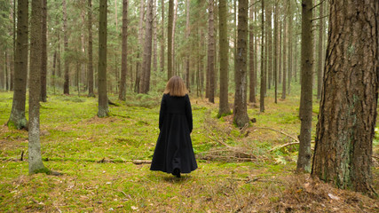 young stylish afro hair woman with a black coat walking in the magical forest, follow camera from back