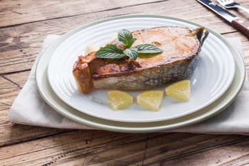 Steak baked fish salmon on a plate with lemon. Wooden table.