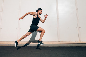 Young man runner running along wall with copy space - Powered by Adobe