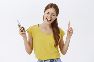 Charming carefree good-looking female in yellow t-shirt wearing wireless earbuds holding smartphone...