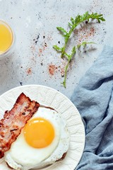 Plate of breakfast with fried eggs, bacon and rye bread toast on a gray background. English breakfast, Orange juice