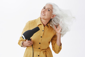 Charming elegant grandmother with grey hair standing in trendy yellow coat bending right, making...