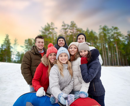 friendship, technology and people concept - group of smiling teenage friends with snow tubes taking picture by smartphone selfie stick outdoors in winter over natural background