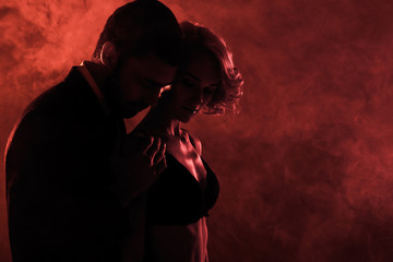 Man tenderly hugging beautiful woman on red smoke background
