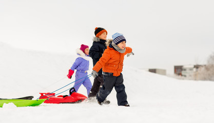 childhood, sledging and season concept - group of happy little kids with sleds in winter