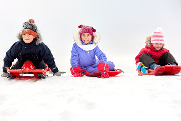 childhood, sledging and season concept - group of happy little kids sliding down on sleds in winter