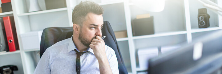 A man sits in a chair in the office and holds a pencil in his hand. On the back of the chair hangs...