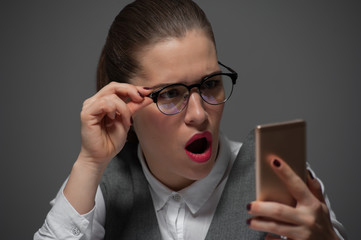 A surprised pretty beautiful businesswoman is holding a phone with a mouth open shocked by the...
