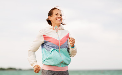 fitness, sport and healthy lifestyle concept - smiling woman running along beach