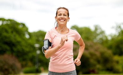 fitness, sport and healthy lifestyle concept - smiling woman with earphones wearing armband for...