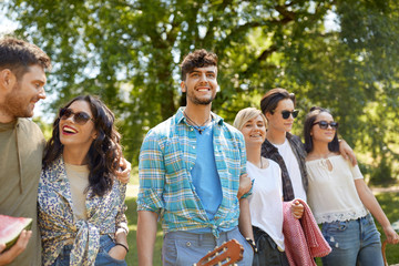 friendship and leisure concept - group of happy friends with guitar and blanket going to picnic at summer park