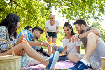 friendship and leisure concept - group of happy friends with non alcoholic drinks and food at picnic in summer park