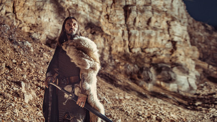 Long haired knight with the two-handed sword. Rocks on the background.