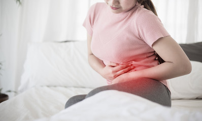 Young asian woman suffering from abdominal pain on the bed.