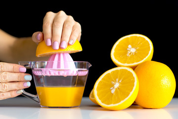 Stylish trendy female manicure. Beautiful young woman's hands on dark background takes juicy oranges on pink background . Manicure concept, juice concept.