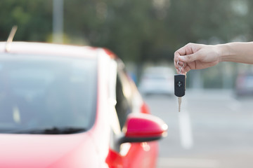 Close up hand of Man holding car key  with blurred red car on background.