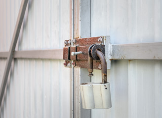 Open padlock that hangs on a rusty latch of the metal gate