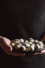 The cook is holding raw quail eggs on black plate 