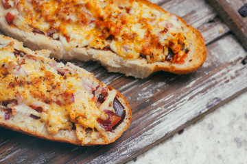 A couple of traditional french split baguettes with cheese and other complex filling. On wooden retro background stand tray.