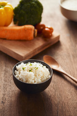 Grains of rice in a wooden bowl and ingredients for a vegetarian recipe - healthy eating concept