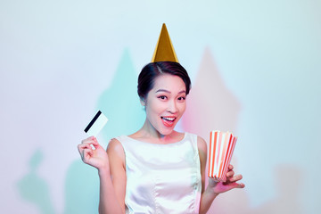 Portrait of young overjoyed attractive woman in white dress watching movie film, holding bucket of popcorn and credit card isolated on white background. Emotions in cinema concept