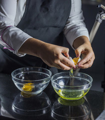 a cook in a black apron separates the yolk from the white in glass bowls on a black background