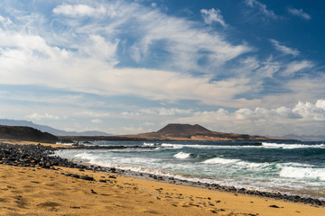 Dramatic seascape with golden beach and waves on a cloudy day on a volcanic island.
