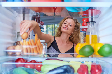 Young Caucasian woman taking egg from fridge to make a breakfast. Picture taken from inside of fridge.