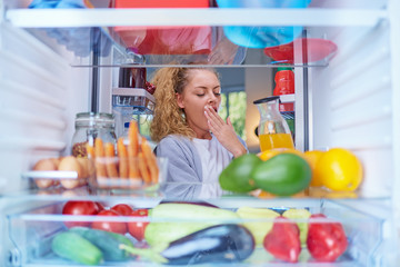 Young Caucasian woman yawning and taking juice from fridge. Morning routine. Picture taken from the inside of fridge.