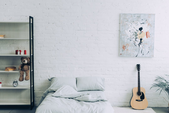 high angle view of modern bedroom with shelves, guitar and painting on white brick wall