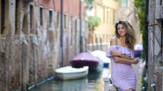Travel tourist woman standing on the pier against beautiful view on venetian chanal with boats in Venice, Italy. Attractive young romantic girl on vacation walking happy by Grand Canal.