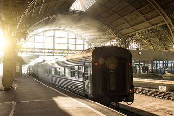 Old retro passenger station in the sun and train composition with a locomotive and a passenger car.