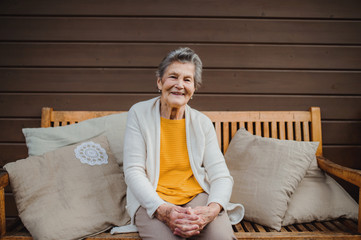 An elderly woman sitting outdoors on a terrace on a sunny day in autumn.