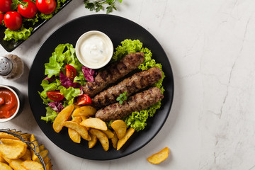 Traditional cevapcici served with baked potatoes. Flat lay. Stone background.