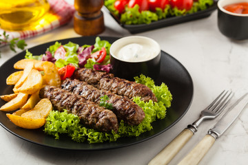 Traditional cevapcici served with baked potatoes. Stone background.