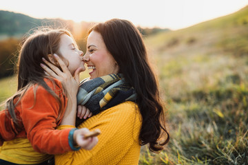 A portrait of young mother with a small daughter in autumn nature at sunset.