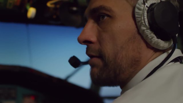 Close up shot of male pilot in headset sitting in cockpit of flying airplane and talking to aircraft captain off camera