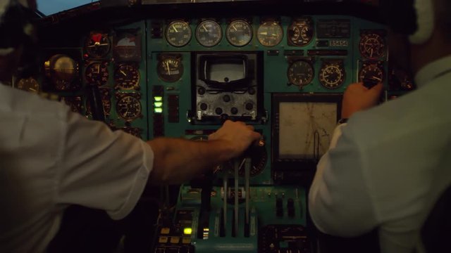 Mid-section shot of unrecognizable pilots in headsets talking and monitoring information on gyroscopic instruments in cockpit while flying airplane