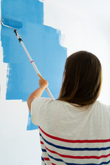 view of woman painting wall of her house in blue color, do it yourself home renovation concept