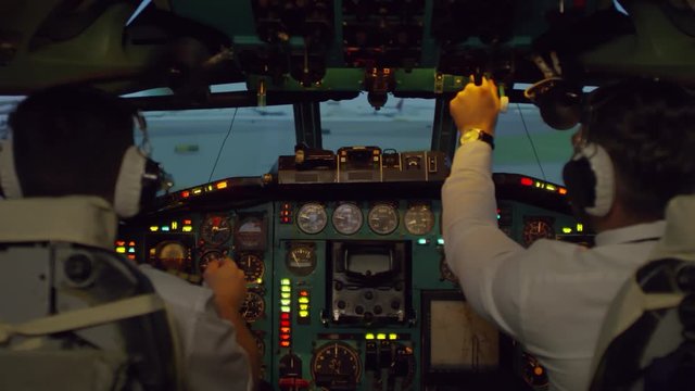 Medium shot of male pilots in headsets operating overhead instrument panel and controlling airplane moving along runway before take-off