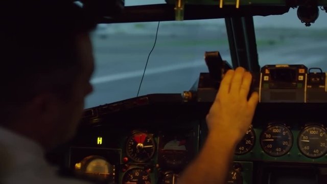 PAN shot of male aircraft captain sitting in cockpit of airplane and operating switches on instrument panel while preparing for flight