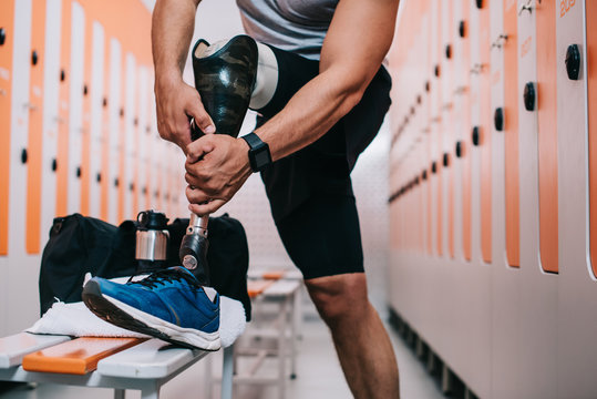 cropped shot of sportsman putting on artificial leg at gym changing room