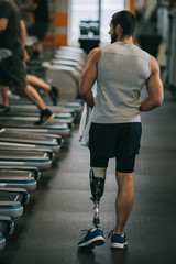 rear view of athletic sportsman with artificial leg walking by gym
