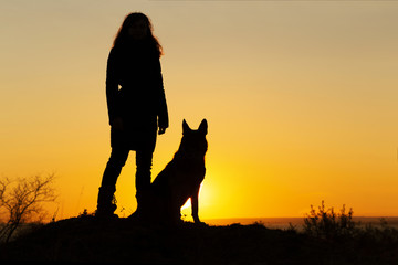 silhouette woman walking with a dog in the field at sunset, a girl in an autumn jacket playing with pet throwing wooden stick on the nature