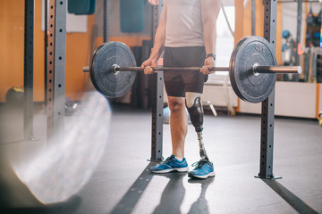cropped shot of sportsman with artificial leg working out with barbell at gym