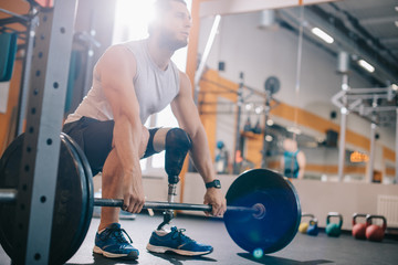 attractive young sportsman with artificial leg working out with barbell at gym